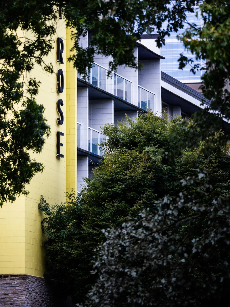 A yellow building with vertical ROSE lettering behind trees.