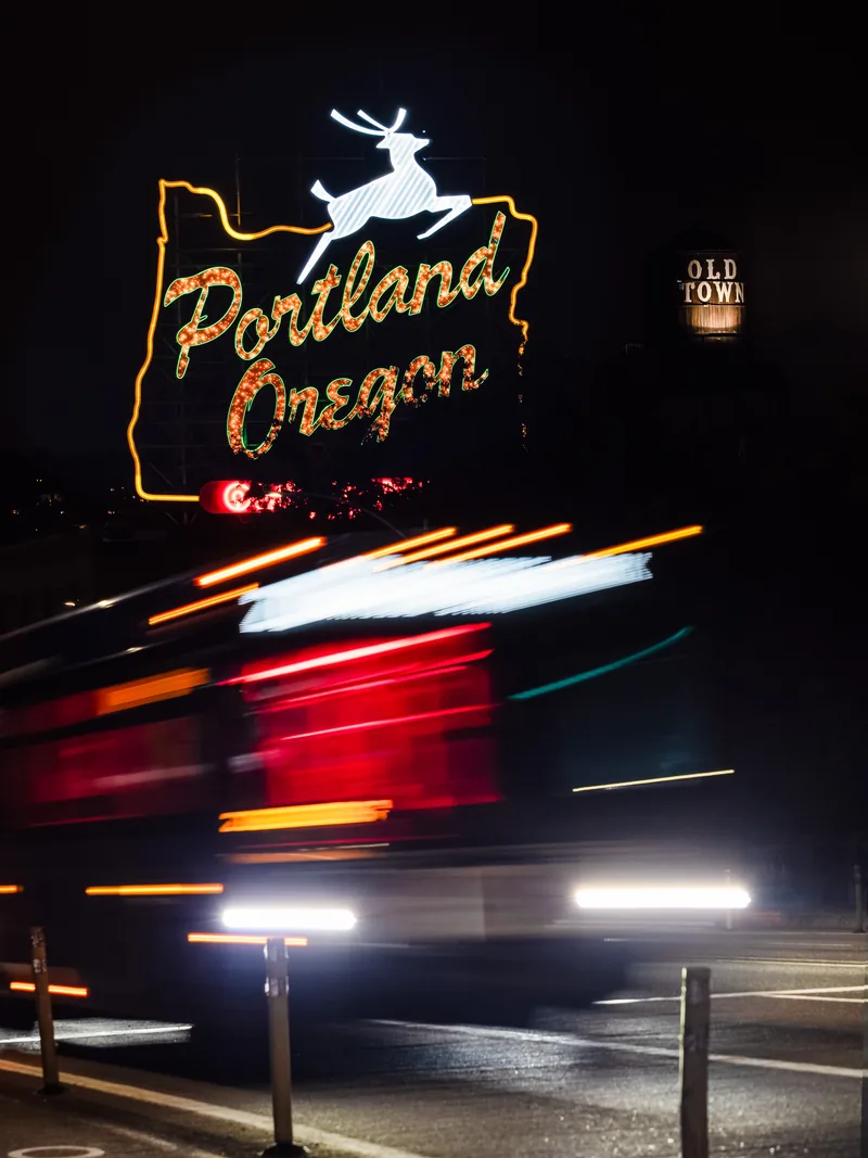 The glowing Portland Oregon stag sign above a streetcar blurred in motion at night.