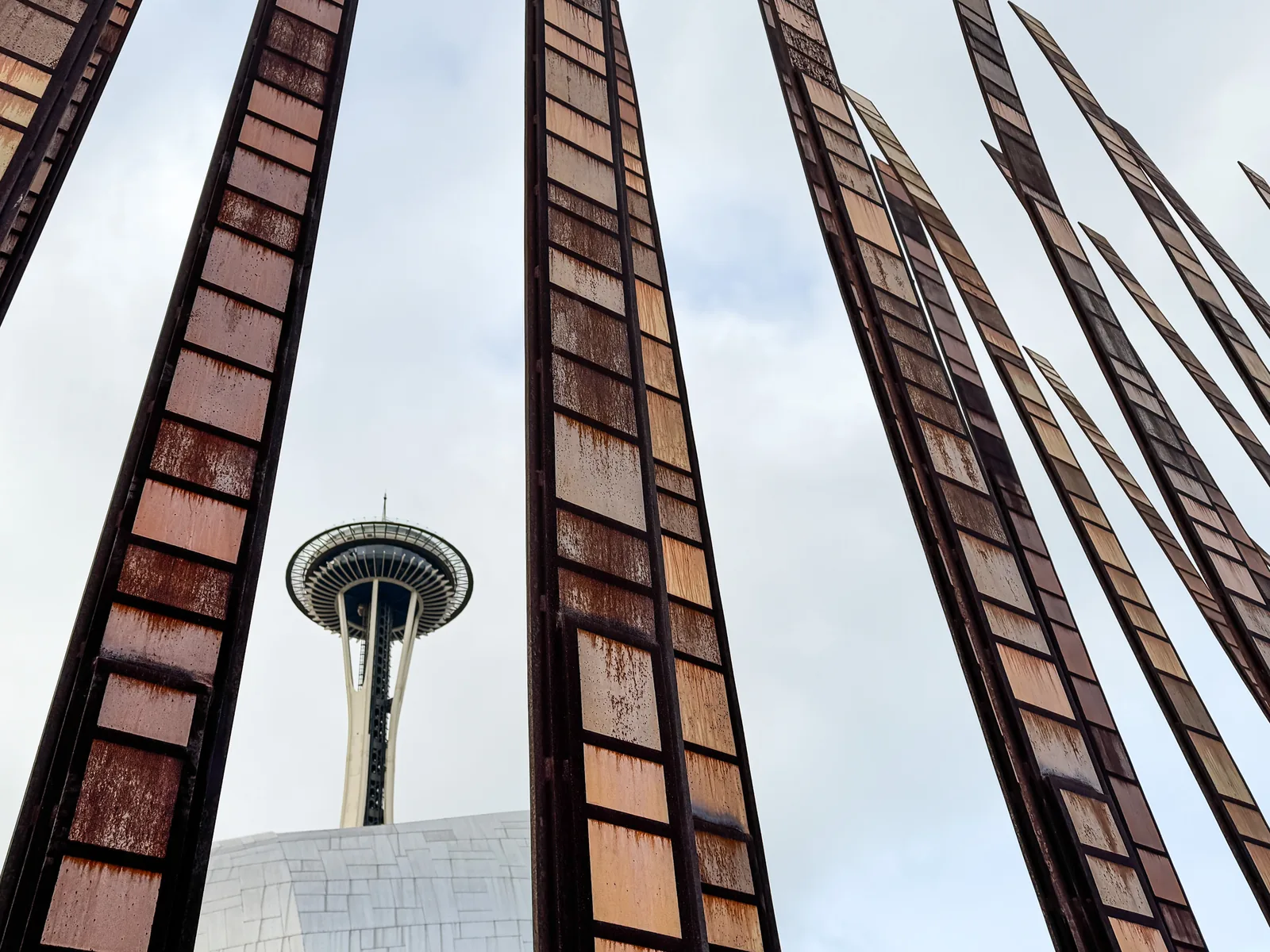 The Space Needle framed between tall rusted steel sculptures against a pale sky.