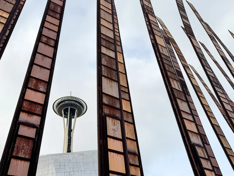 The Space Needle framed between tall rusted steel sculptures against a pale sky.