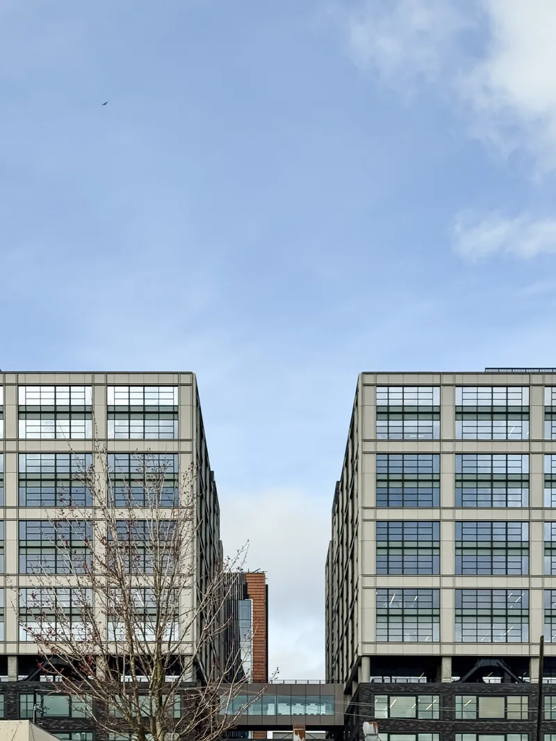 Two matching office buildings with a narrow gap of blue sky between them.