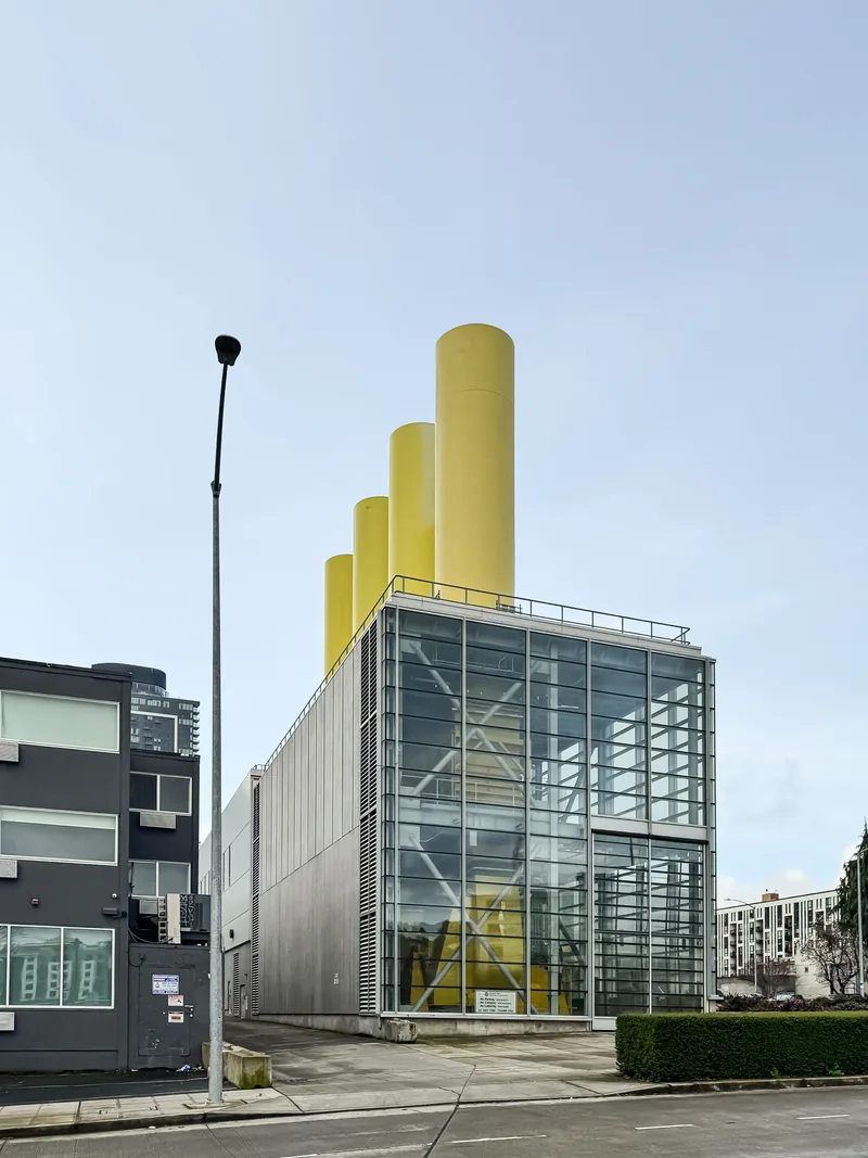 A glass building with bright yellow smokestacks beside a street lamp.