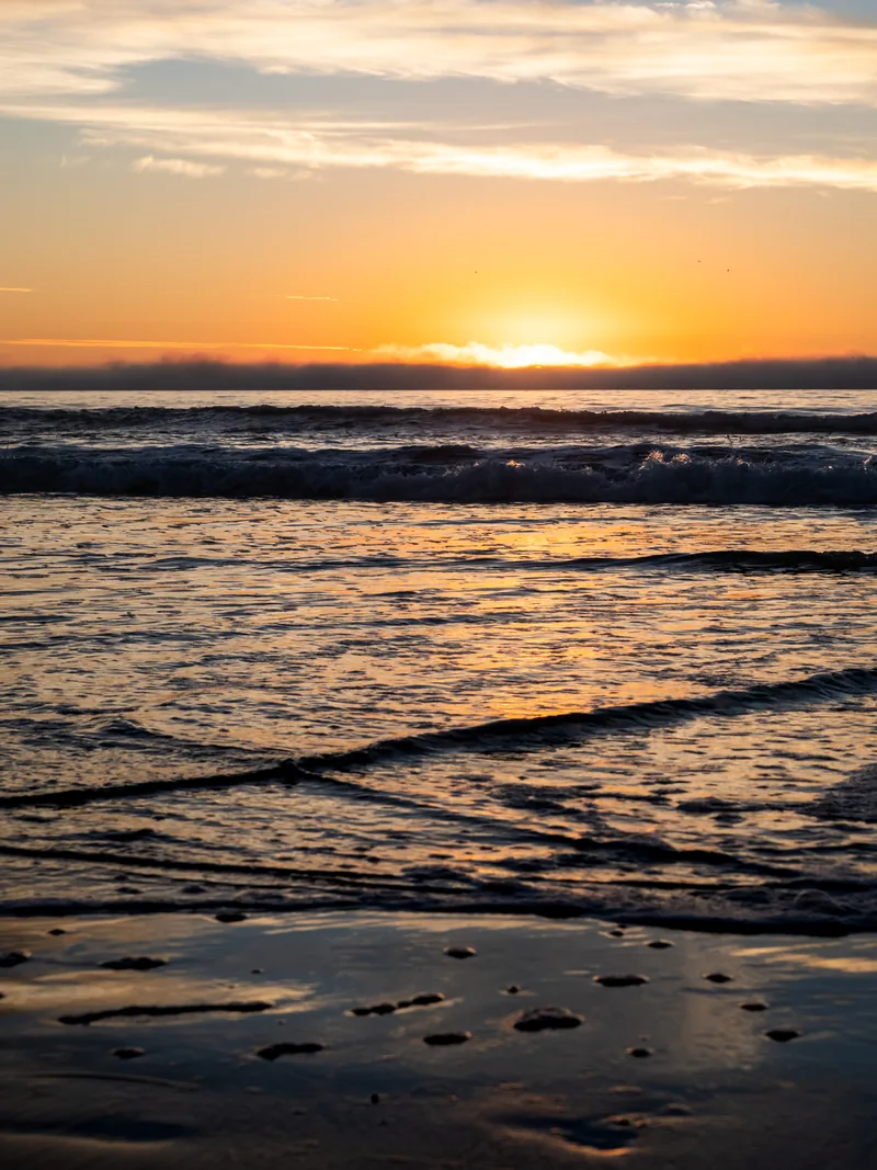 The sun setting over gentle waves and a glossy wet beach.