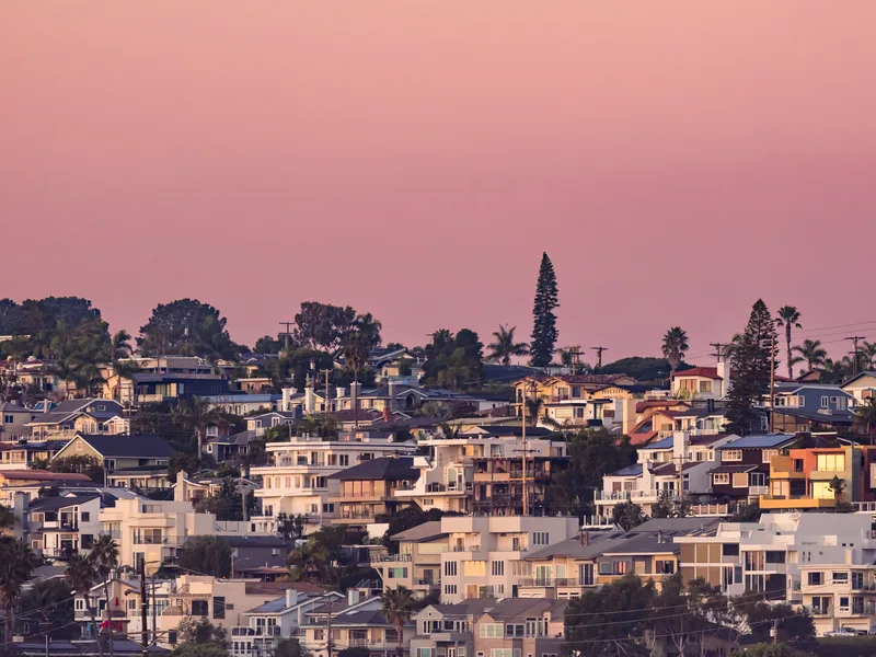Hillside homes glowing in warm light under a pink sky.