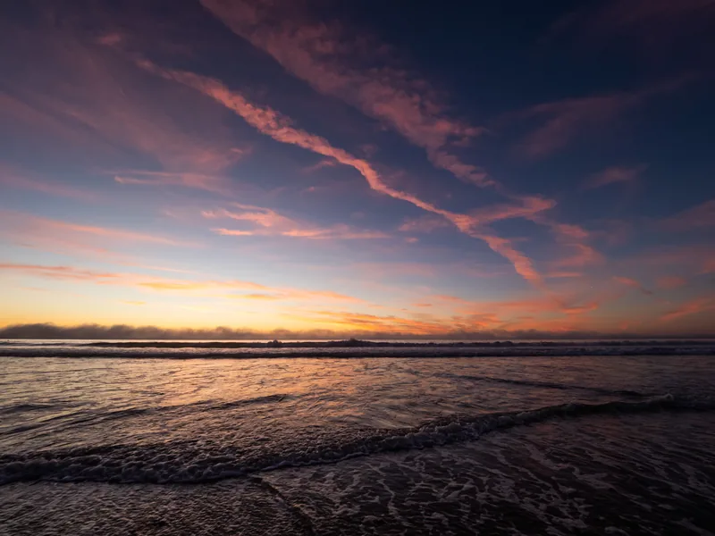 Streaks of pink and orange cloud over the ocean at dusk.