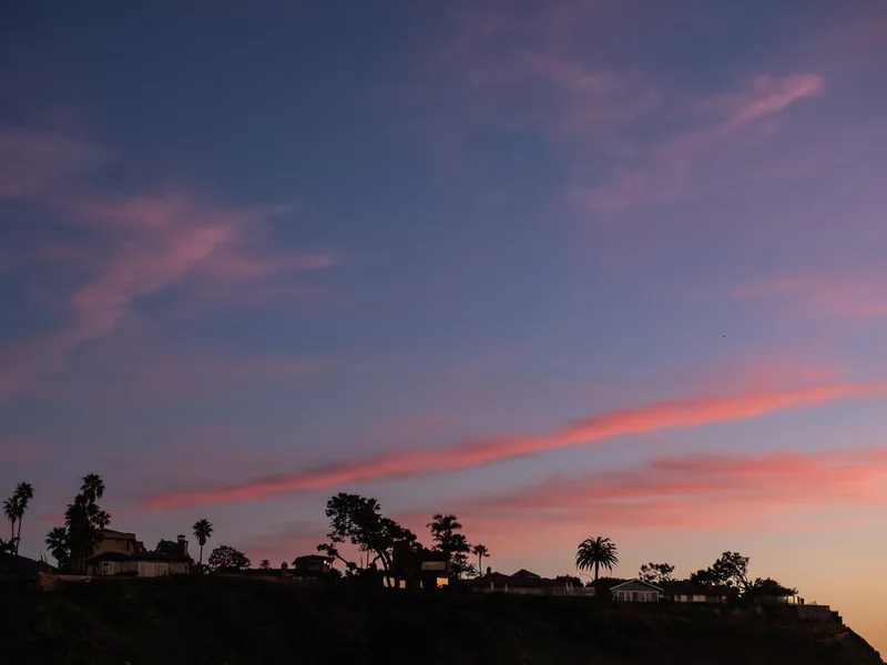Clifftop trees and houses silhouetted against a colorful evening sky.
