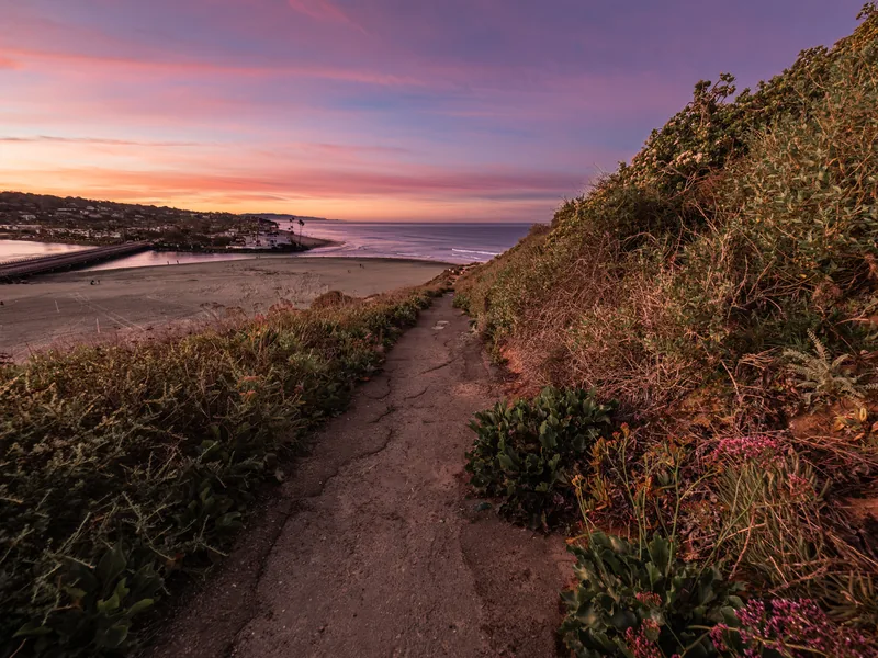 A dirt trail along a bluff above the beach at sunrise.