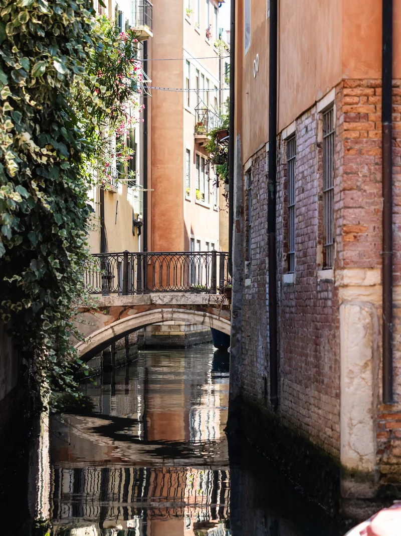 A narrow canal between old brick walls, with a small bridge and ivy reflected in the water.