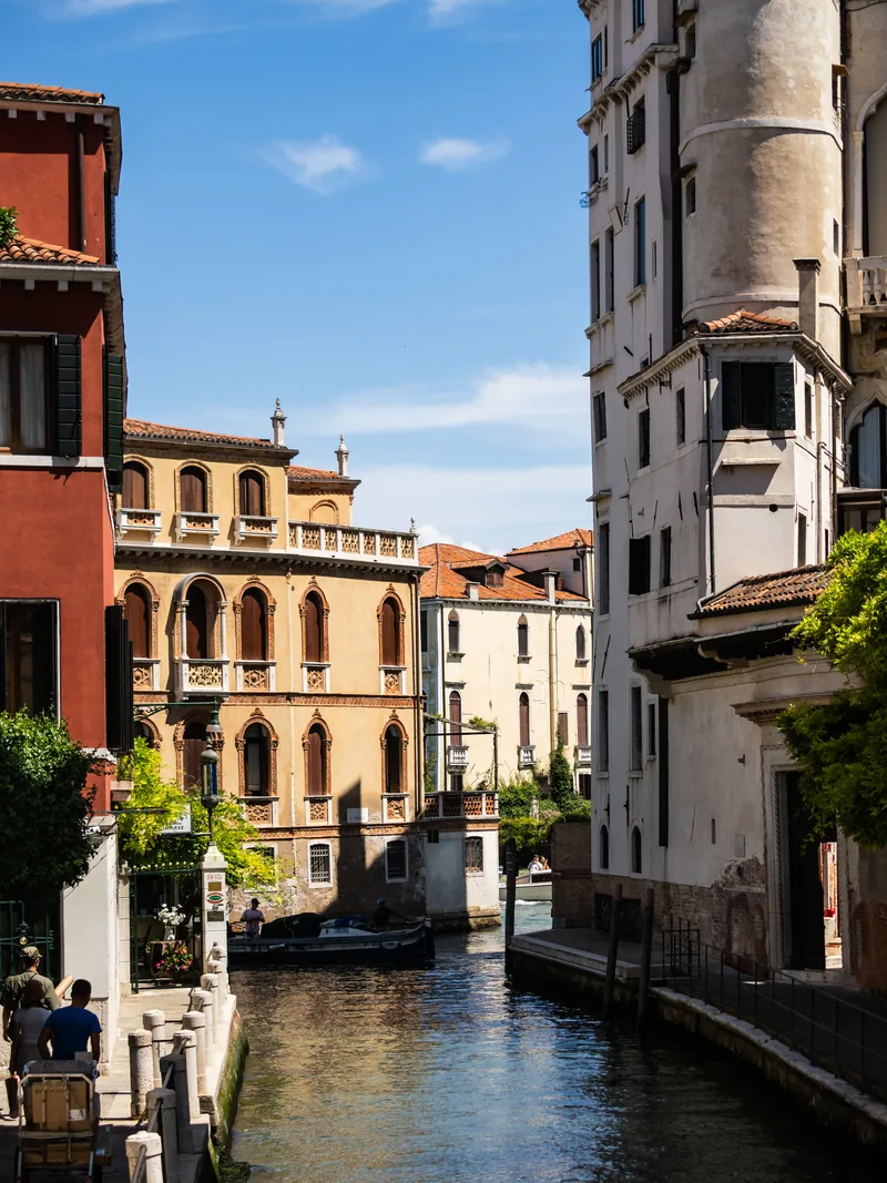 A canal between pastel and red buildings leading to an ornate palazzo in the distance.