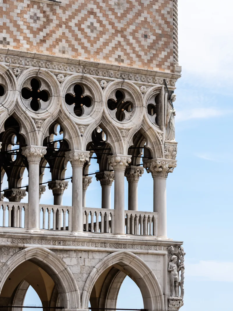 The white Gothic tracery and quatrefoil windows of the Doge's Palace against a pale sky.