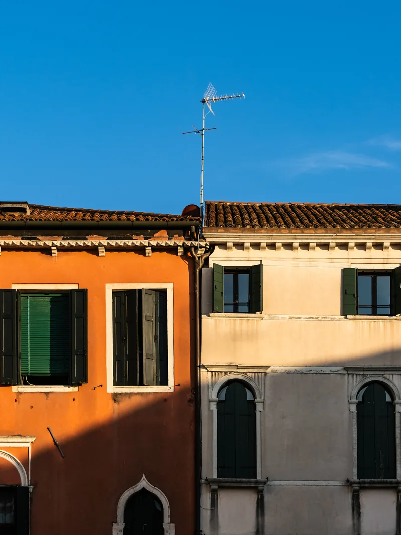 Orange and cream façades with green shutters under a deep blue sky and a lone TV antenna.
