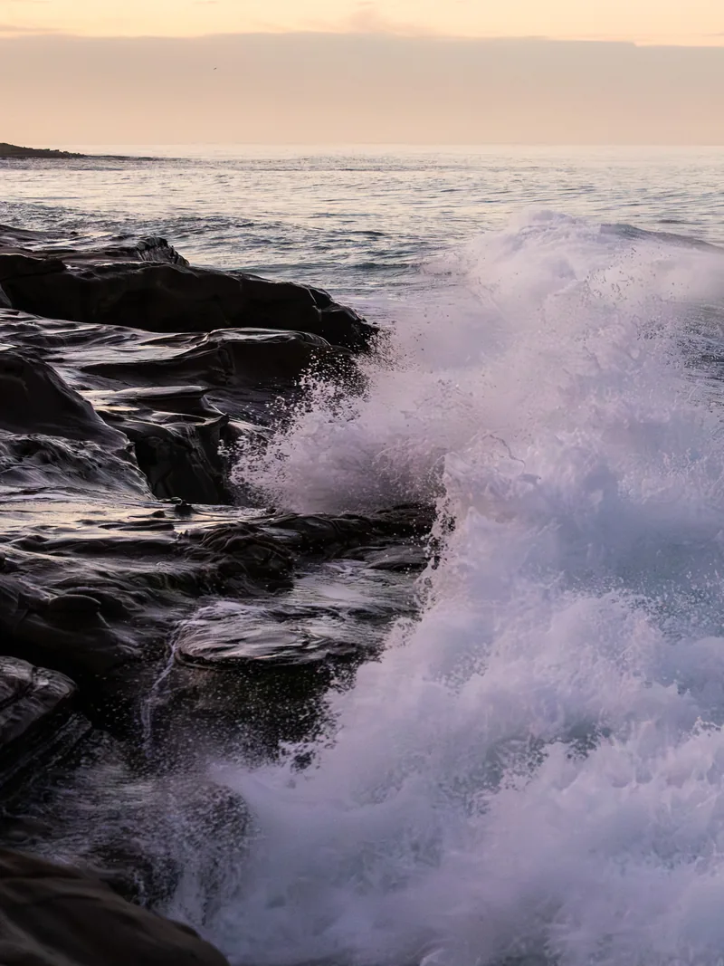 A big wave exploding over dark rocks.