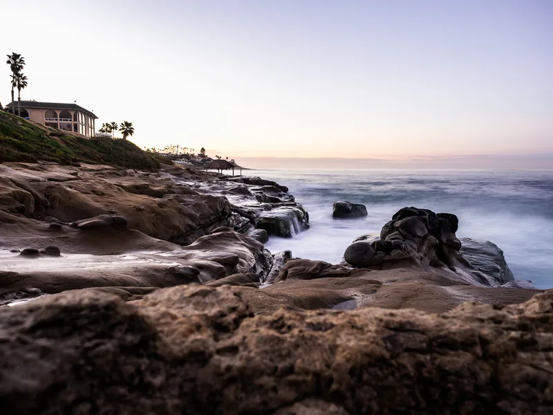 Rocky shoreline and a house on the bluff in soft early light.