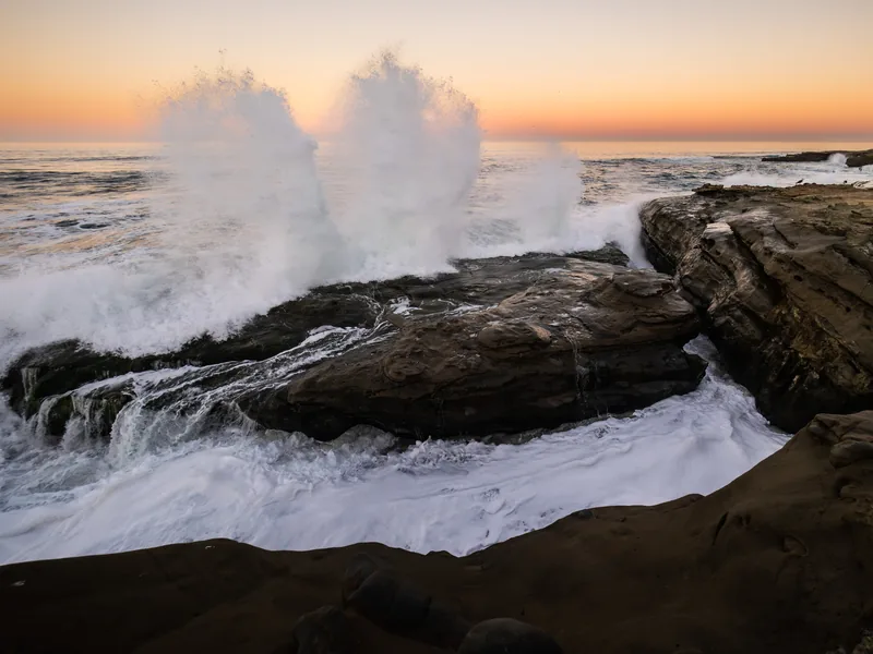 Surf crashing over rock shelves under an orange horizon.
