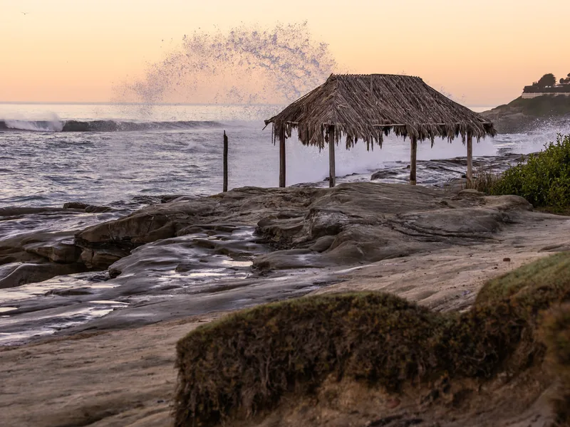 Spray rising behind the thatched Windansea shack at sunrise.